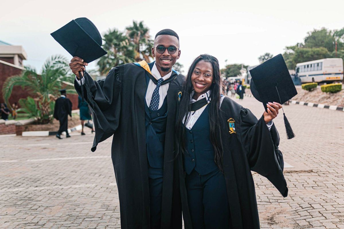 Two graduates in academic gowns, smiling and holding their caps