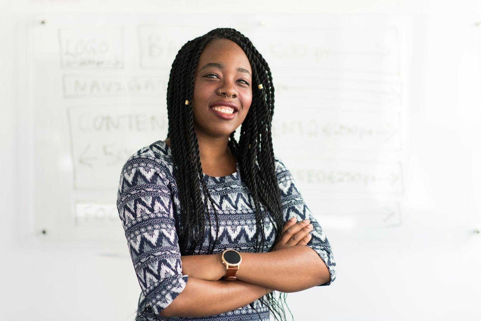 A smiling professional standing with her arms crossed in front of an office whiteboard